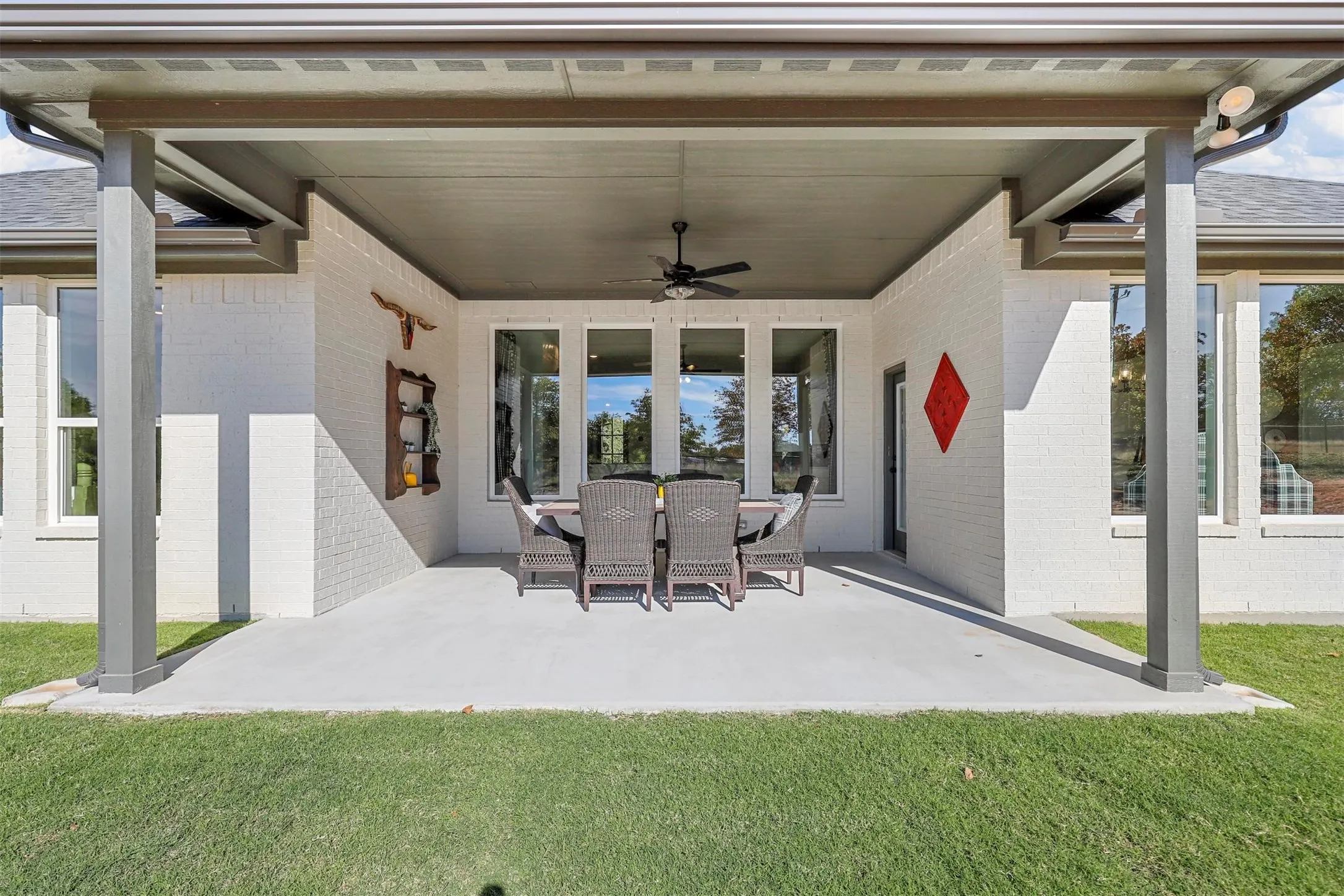 Covered patio with a ceiling fan, white brick exterior, multiple large windows, and a glass-paneled door