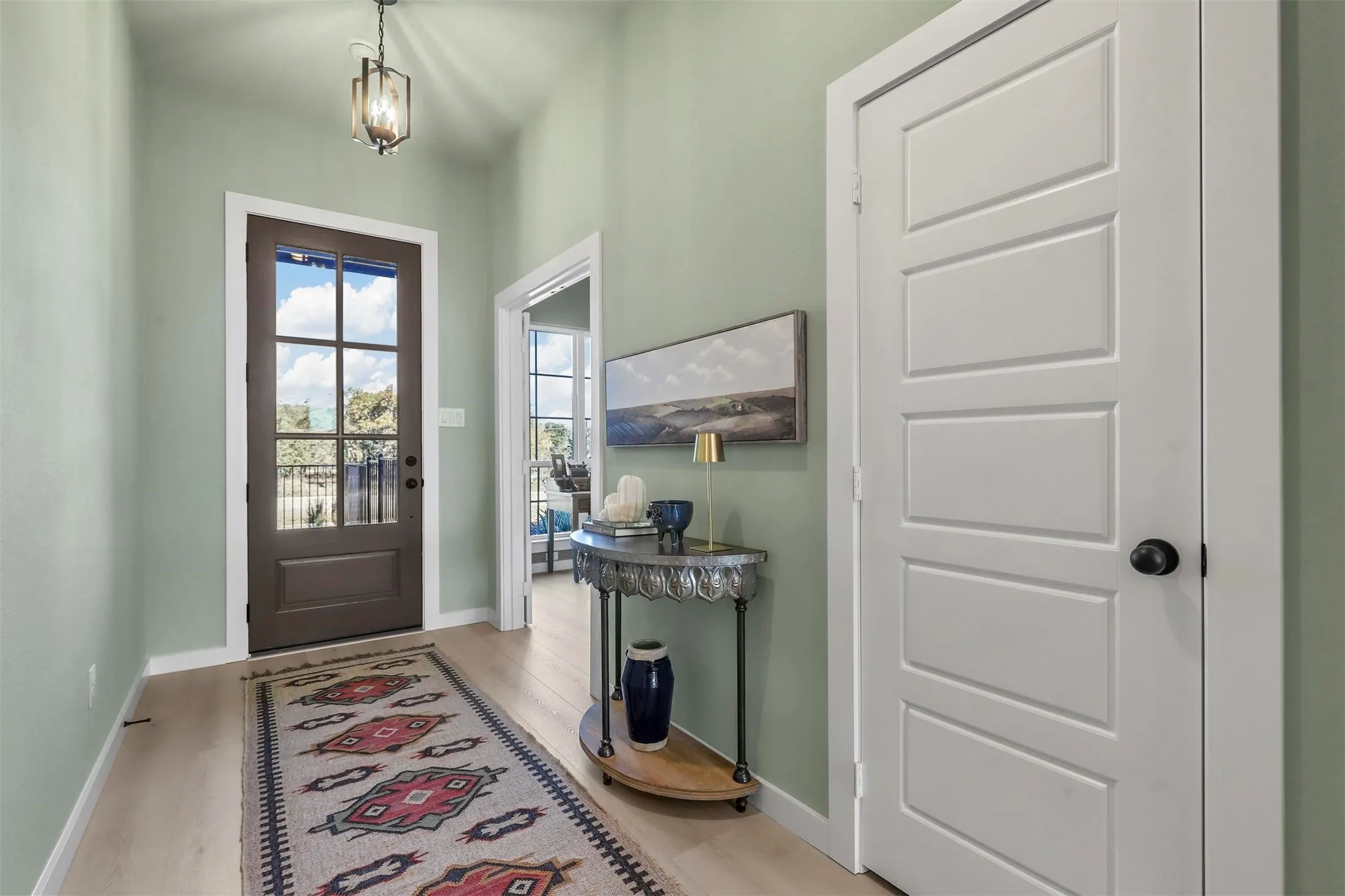 Entryway featuring a dark wood-finish door with glass panels, light wood-finish flooring, and a decorative pendant light fixture