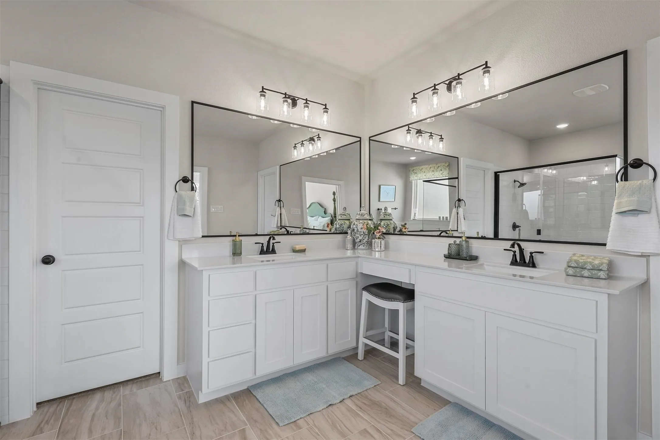 Dual white vanities with integrated sinks, white countertops, black-framed mirrors, and wood-finish flooring