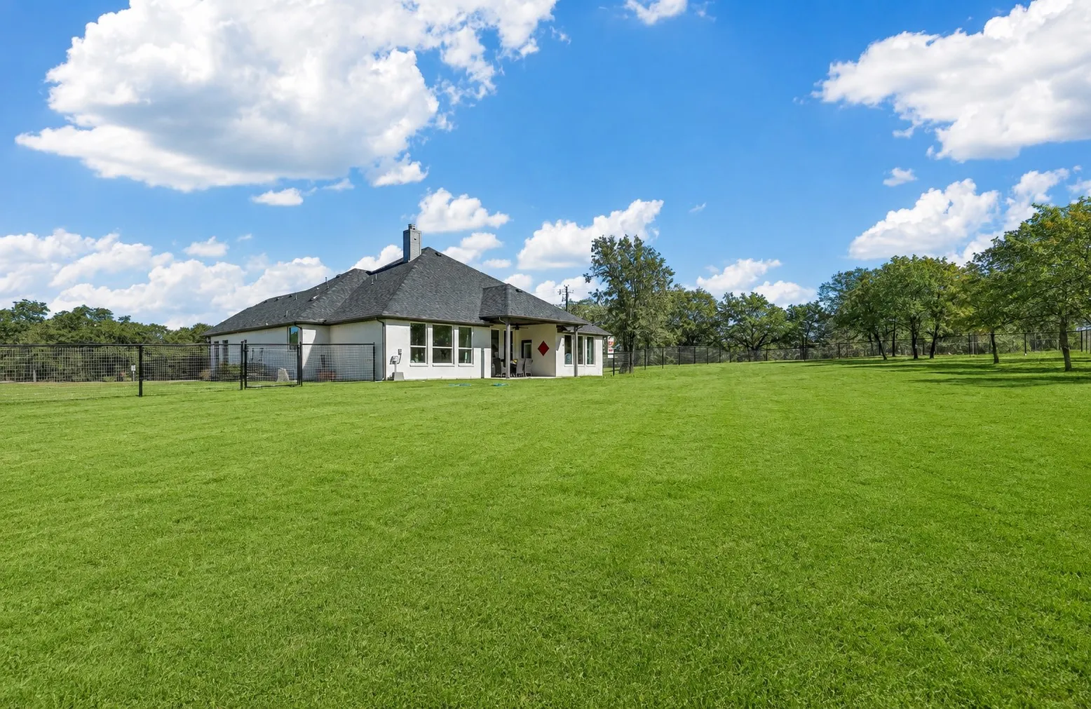 Expansive green lawn with mature trees, a single-story residence with a dark shingle roof, and multiple windows