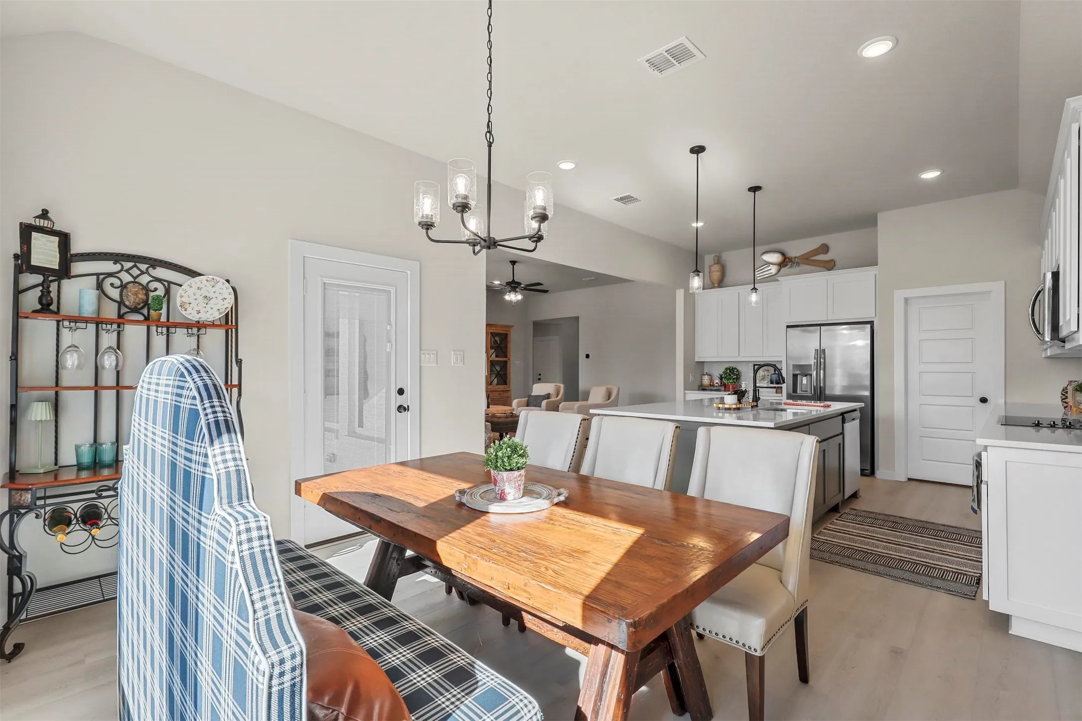 Vaulted ceiling, wood-finish flooring, white shaker cabinetry, stainless steel appliances, and a kitchen island with seating