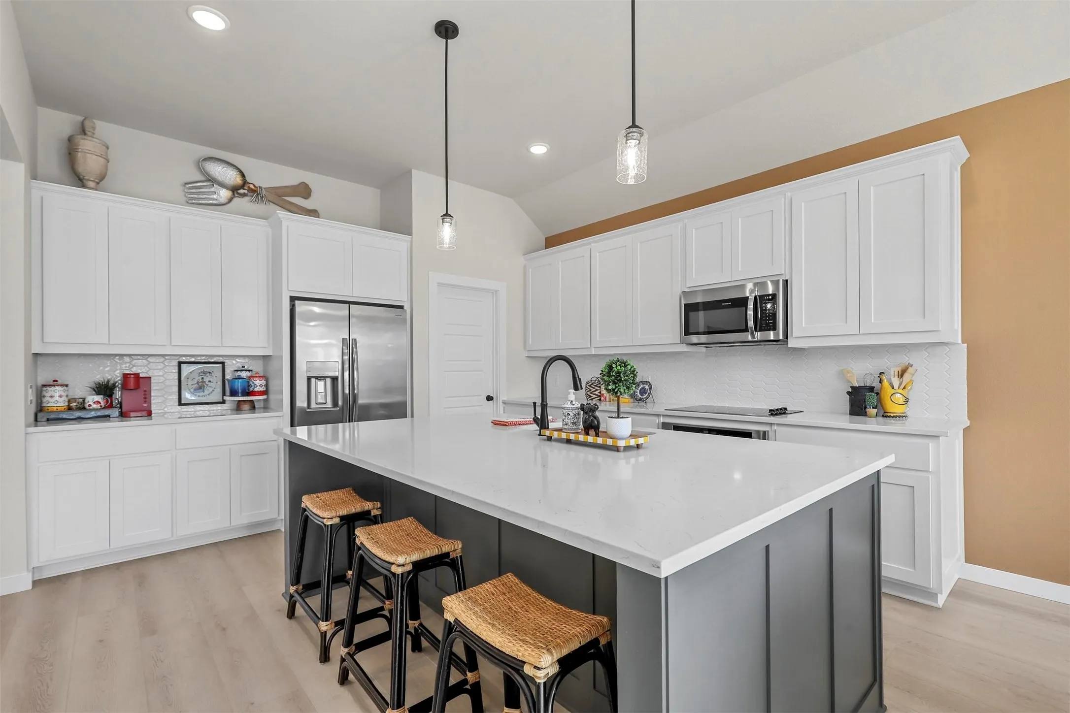 Spacious kitchen featuring white shaker cabinetry, stainless steel appliances, a large island with a light-colored countertop, and a tile backsplash