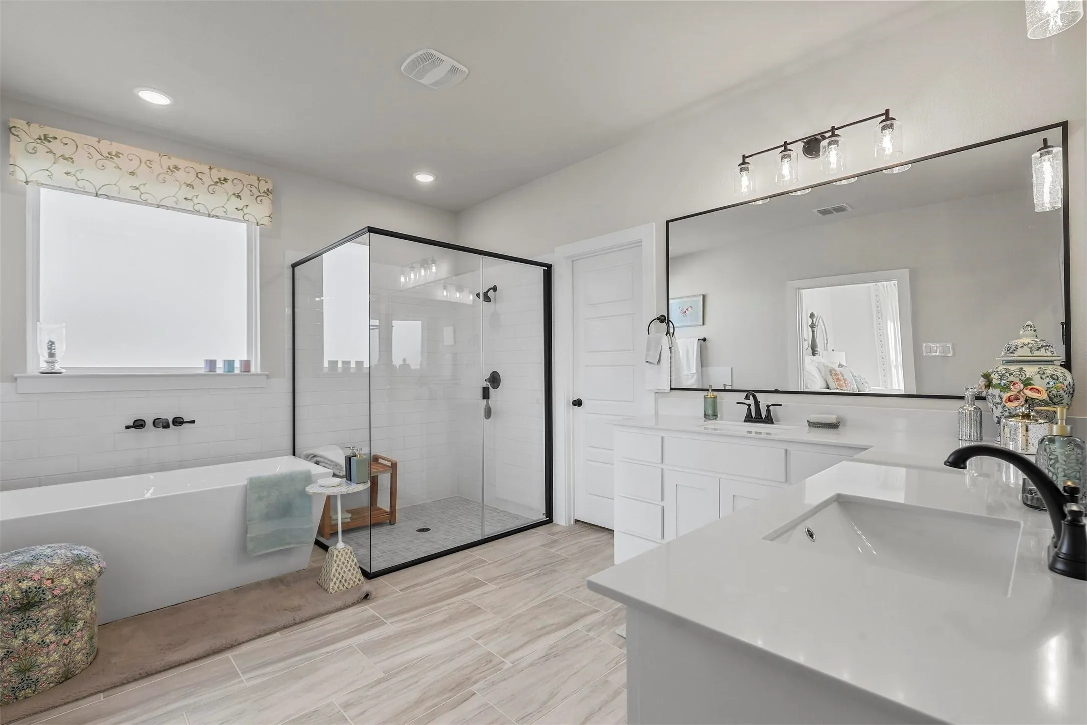 Freestanding soaking tub with matte black fixtures, glass-enclosed shower with matte black fixtures, dual vanity with undermount sinks and light countertops, and wood-finish flooring