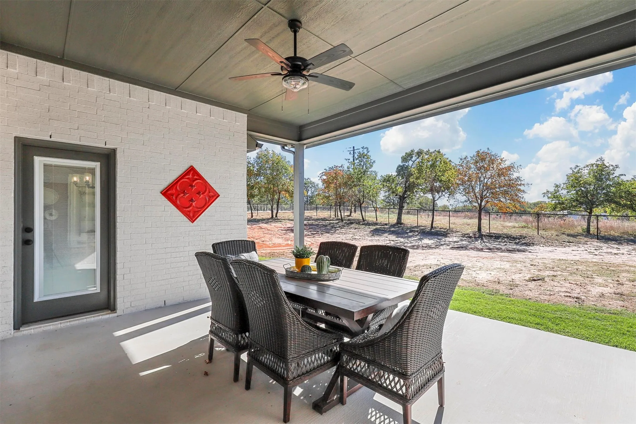 Covered patio with a ceiling fan, white brick exterior, concrete flooring, and a glass-paneled exterior door