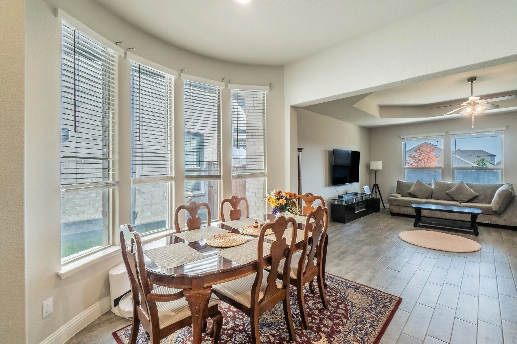 Bay window with multiple vertical blinds, recessed ceiling lighting, wood-finish flooring, tray ceiling with a mounted ceiling fan, and large windows