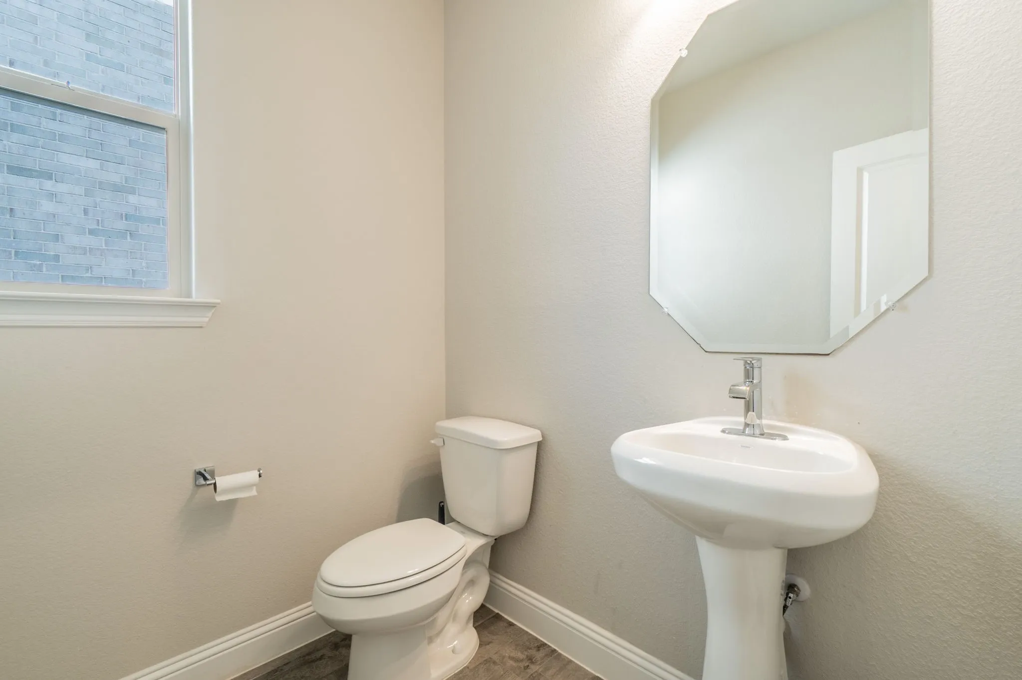 Pedestal sink with polished chrome faucet, octagonal mirror, toilet, and window with trim