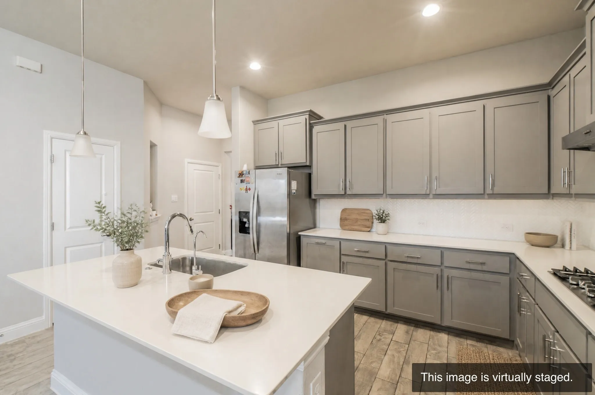 Kitchen featuring a central island with an undermount sink, pendant lighting, gray shaker-style cabinetry, stainless steel appliances, and wood-finish flooring