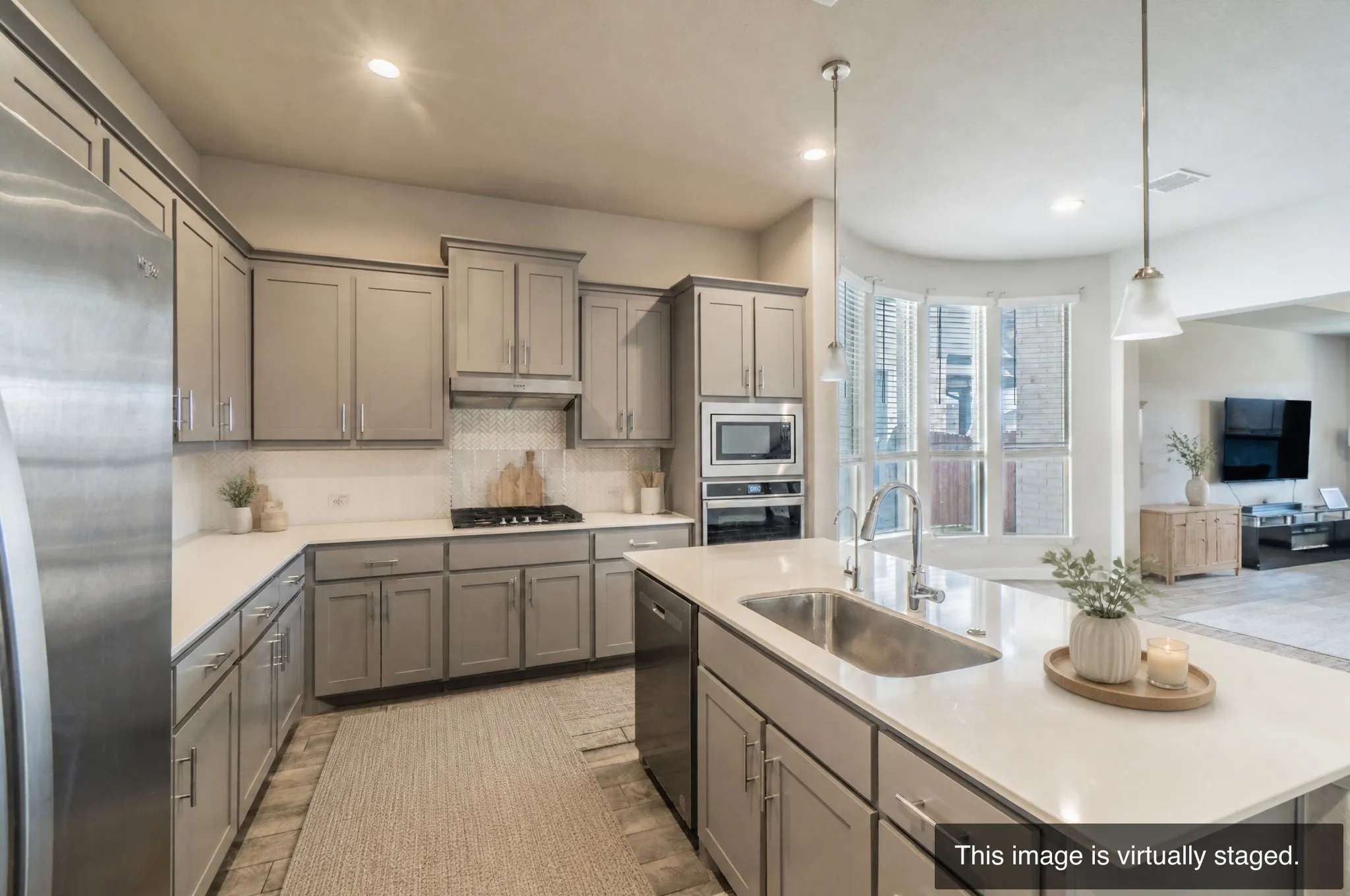 Kitchen featuring a central island with an undermount sink, pendant lighting, white countertops, stainless steel appliances, and gray cabinetry