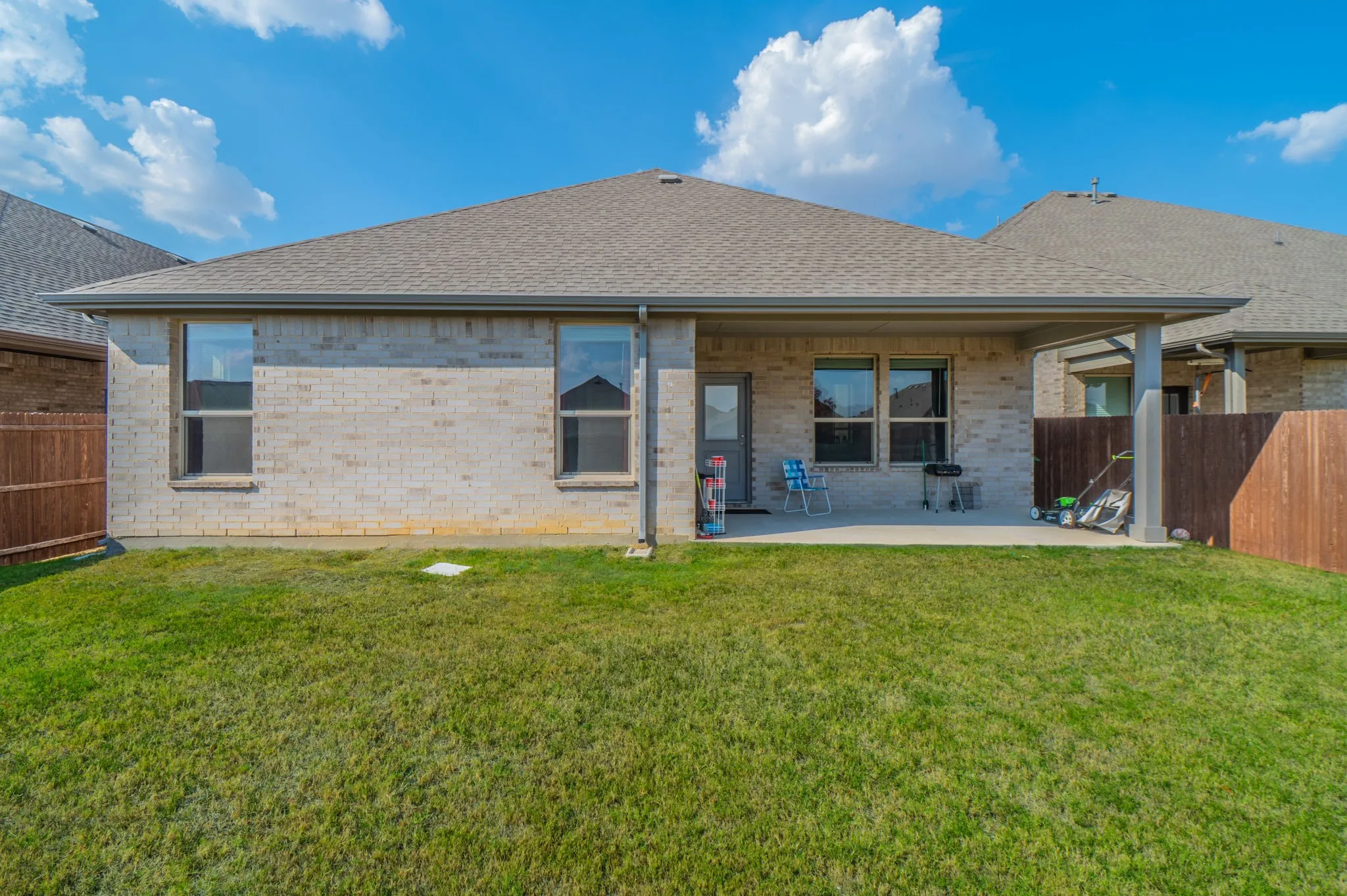Brick exterior with a covered patio, shingle roof, and a fenced yard