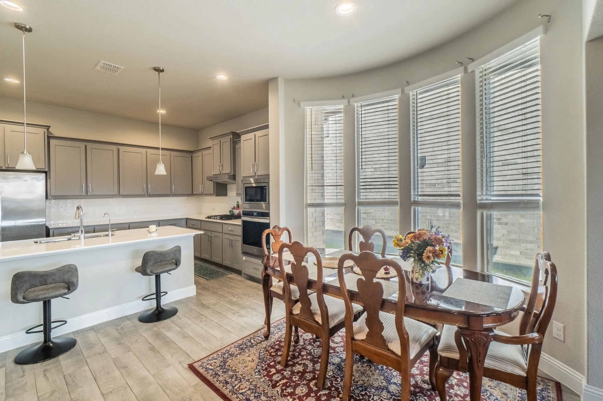 Kitchen and dining area featuring wood-finish flooring, recessed lighting, pendant lighting, built-in stainless steel appliances, and a curved wall of windows