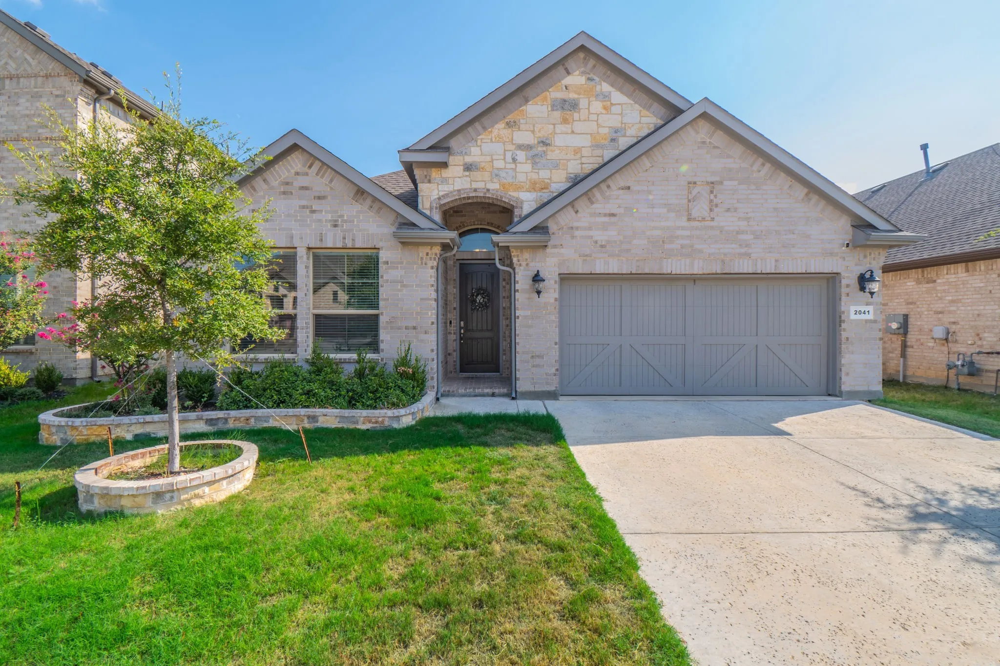 Stone and brick facade with an arched entry, a concrete driveway, and an attached garage with carriage-style doors