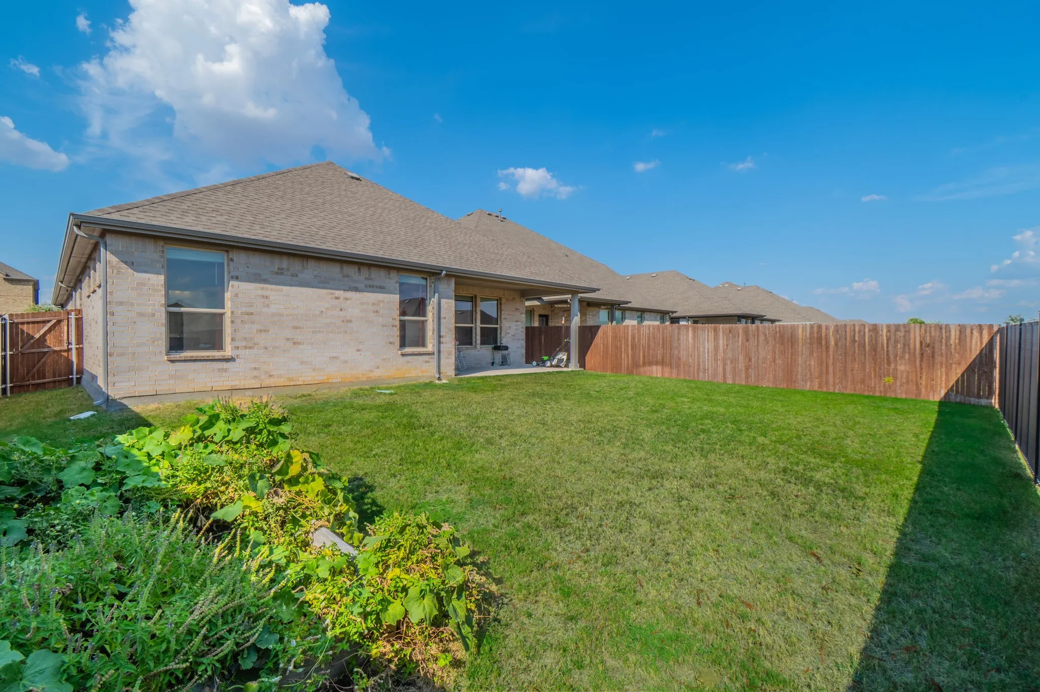 Expansive green lawn with a solid wood privacy fence, brick exterior, and covered patio