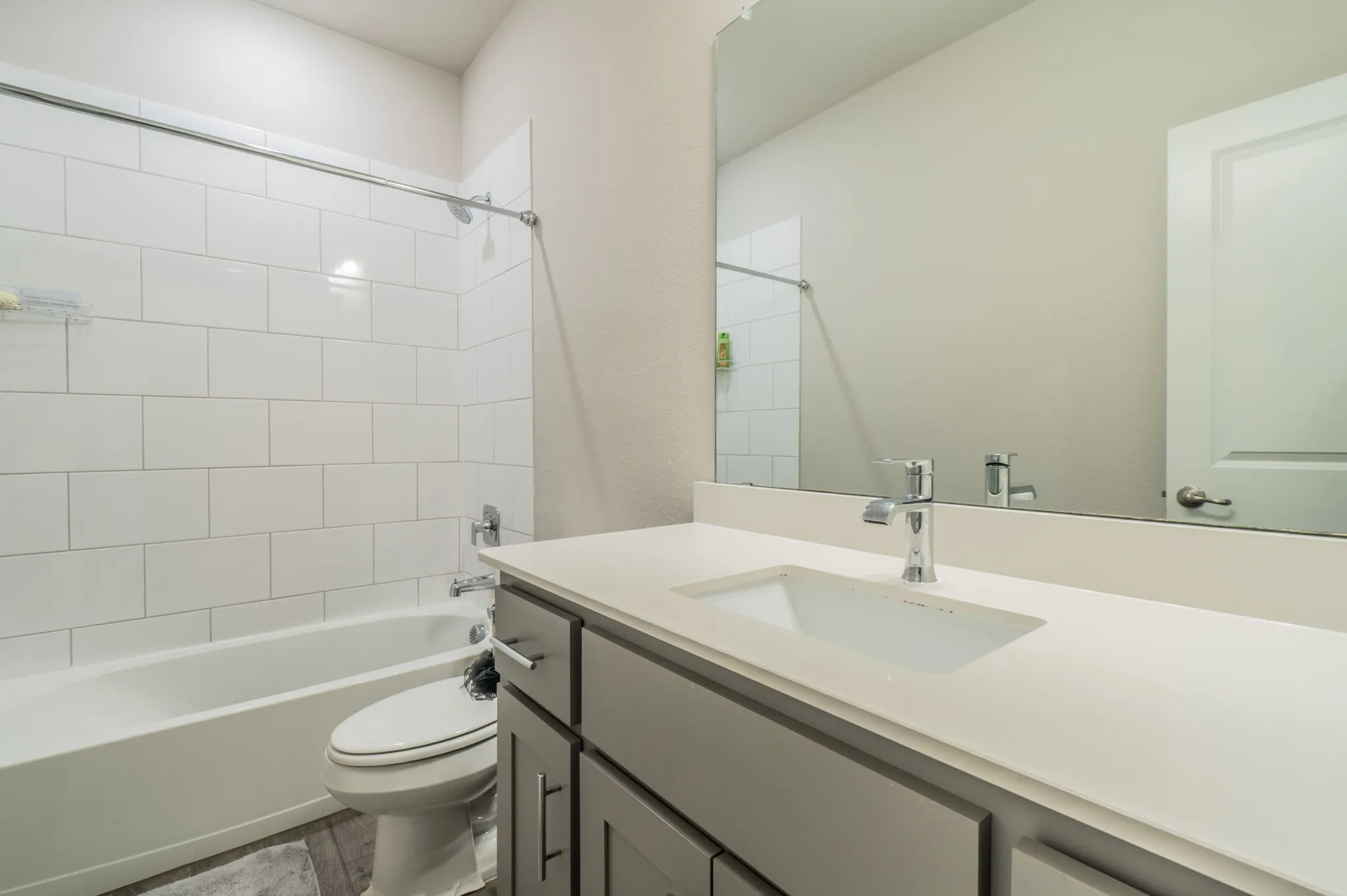 Bathroom featuring a white subway tile shower, white bathtub, gray vanity with an integrated sink, and a chrome faucet