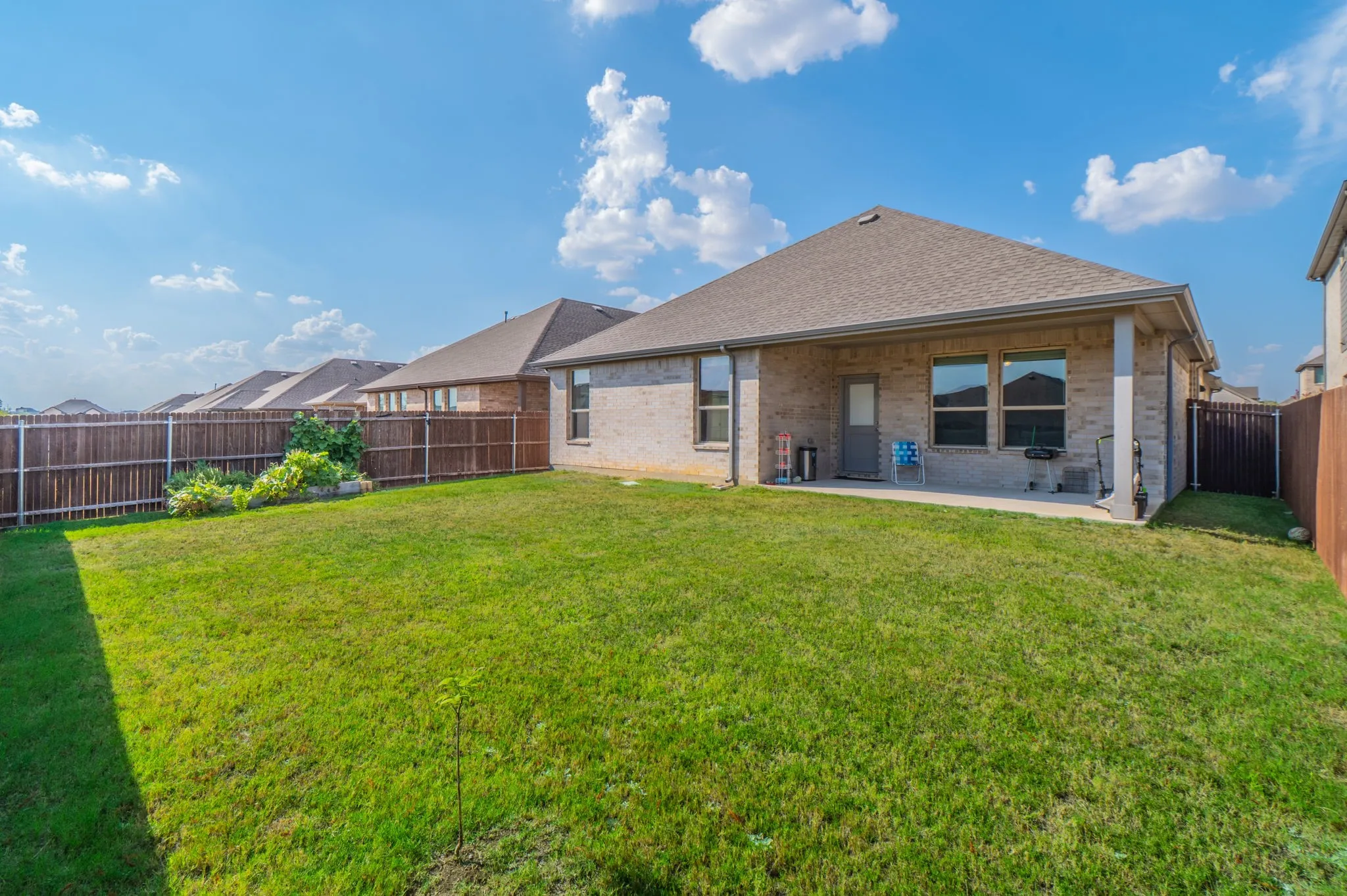 Expansive rear yard featuring green lawn, wood fencing, and a covered concrete patio