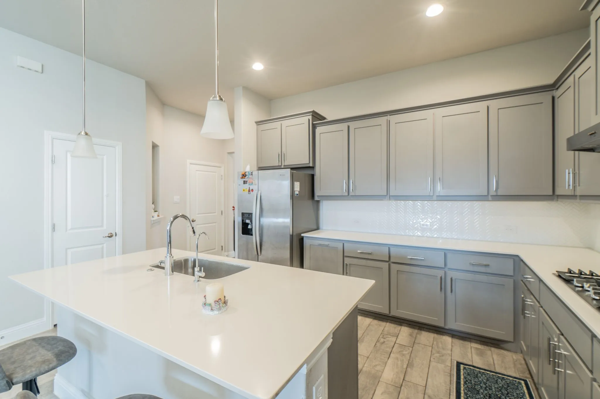 Kitchen featuring light gray cabinetry, white countertops, stainless steel appliances, a white herringbone tile backsplash, and wood-finish flooring