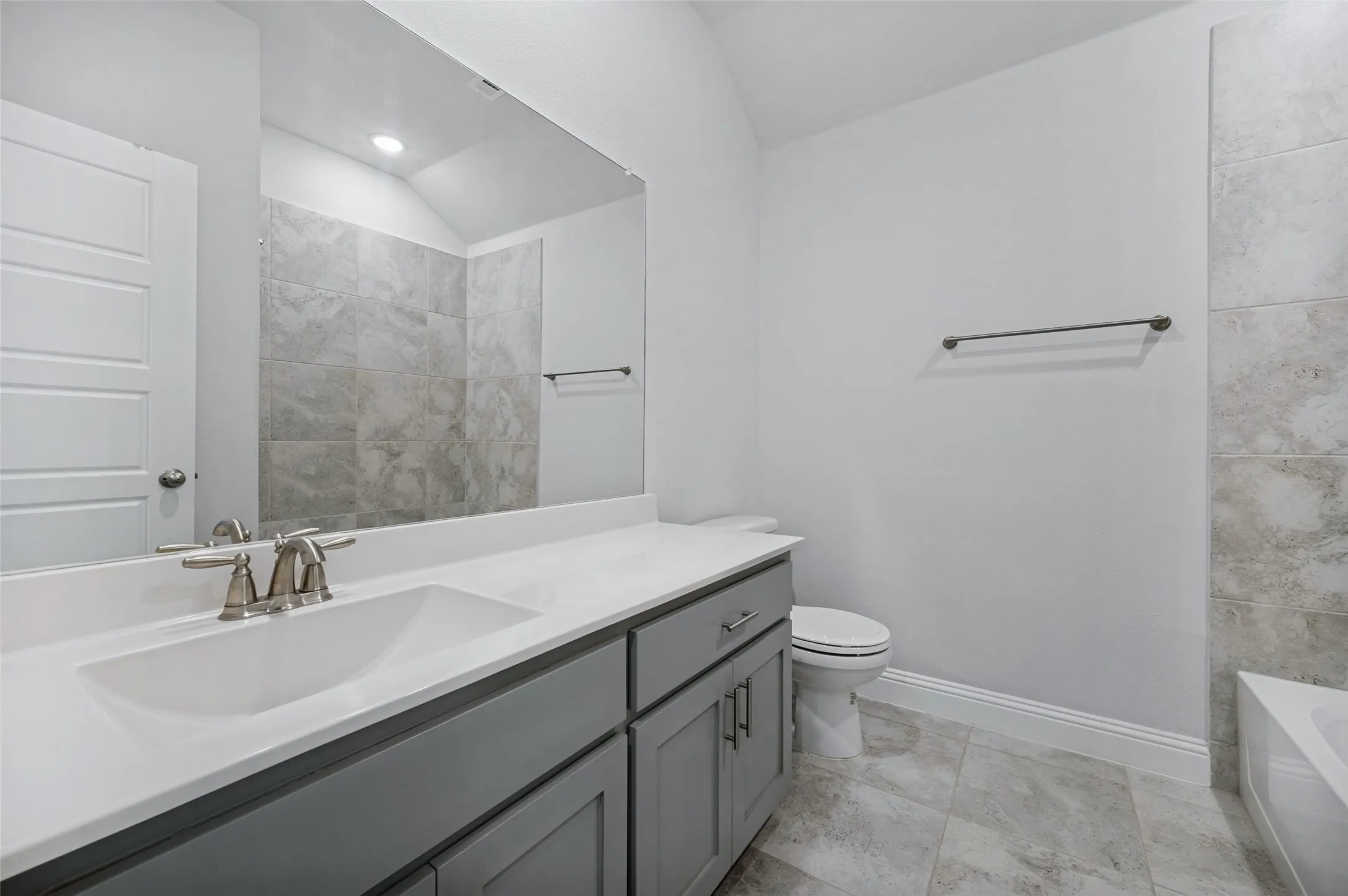 Upstairs bathroom has vanity with an integrated sink, brushed nickel fixtures, a large mirror, tiled flooring, full size bathtub.