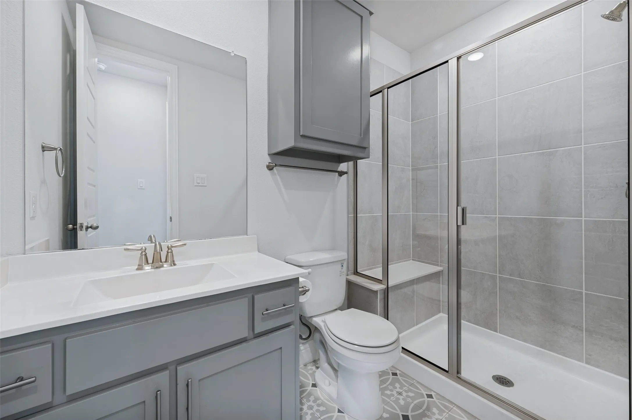 Downstairs full bath with step in shower, vanity with light-toned countertop, integrated rectangular sink, gray cabinetry, and decorator tile flooring.