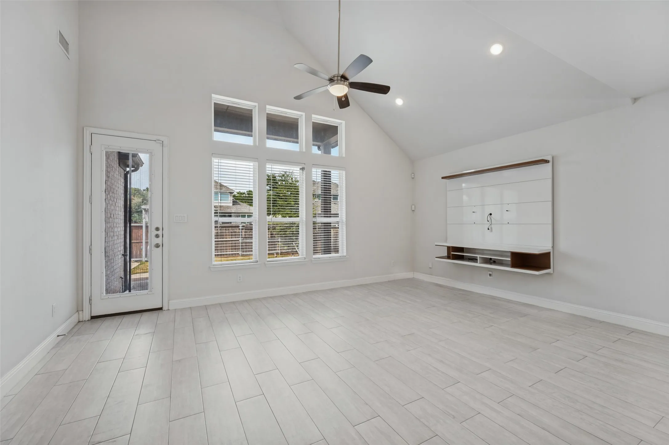 Vaulted ceiling with a ceiling fan, recessed lighting, tile flooring, a wall-mounted media console, and a glass-paneled exterior door. Lots of light!
