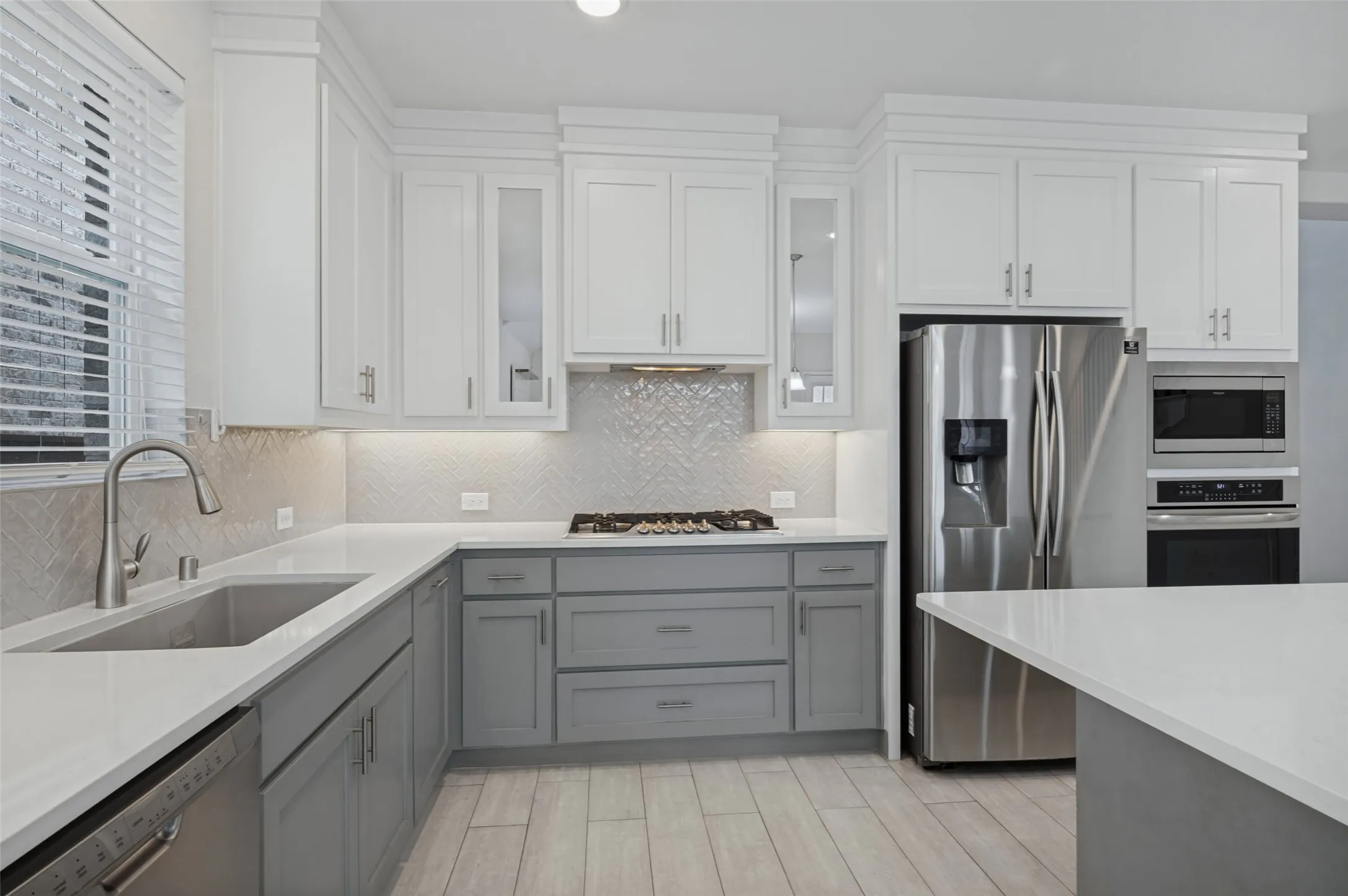 Modern kitchen with two-tone cabinetry, stainless steel appliances, a gas cooktop, and light-toned tile flooring.
