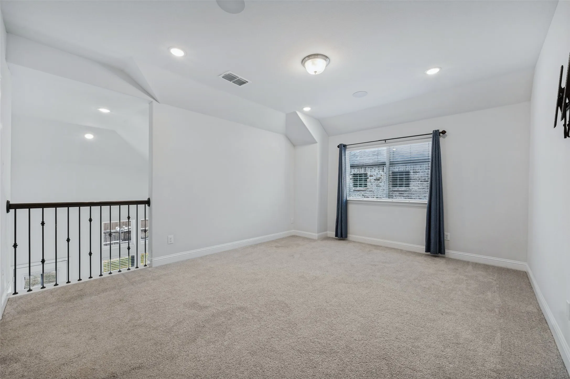 Upstairs den/office/play/flex room featuring carpeted flooring, recessed lighting, ceiling-mounted light fixture, and wrought iron railing overlooking living room below.