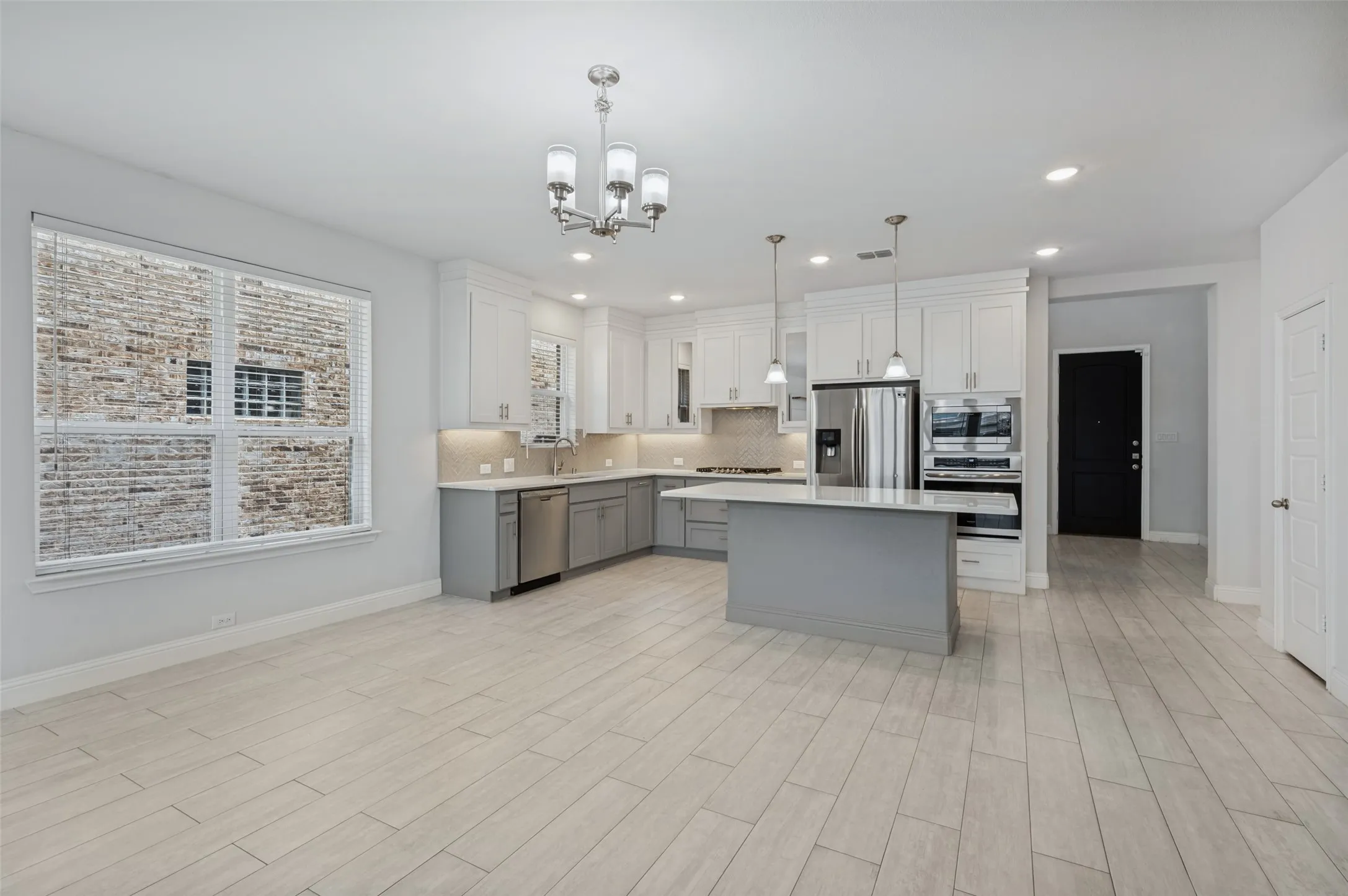 Open-concept kitchen with a central island, ceramic tile flooring, recessed lighting, and stainless steel appliances. Room for large dining table. Pantry door to right.