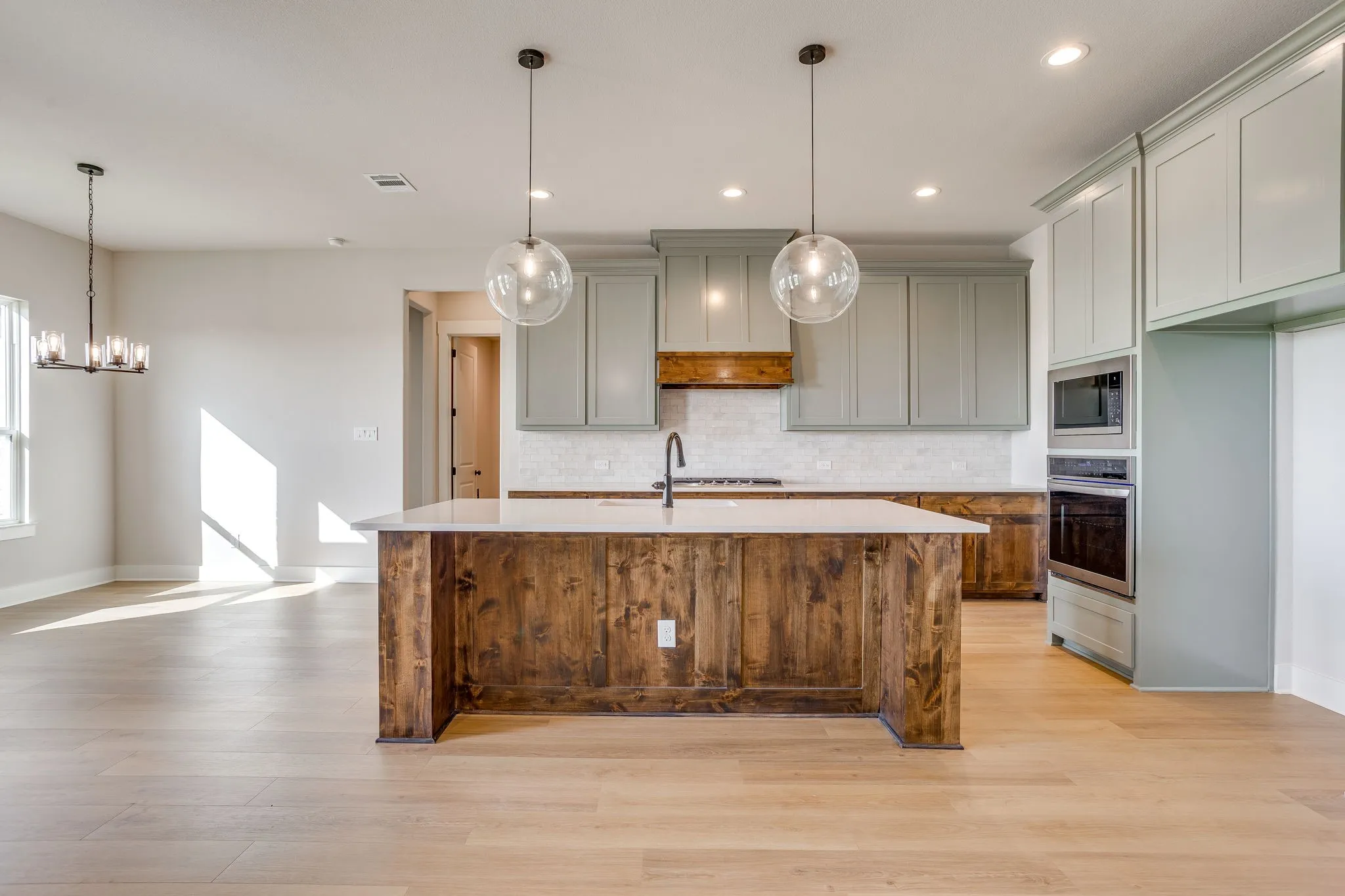 Spacious kitchen featuring an island with wood-finish paneling and light countertop, light green cabinetry, integrated stainless steel appliances, and wood-finish flooring