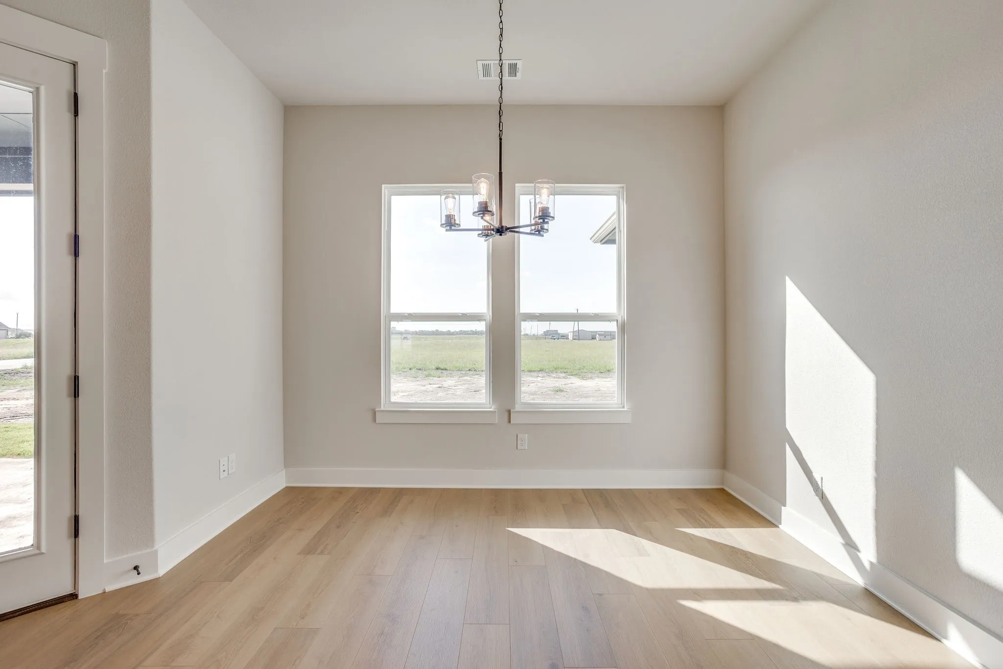 Light wood-finish flooring, dual windows, and a chandelier with seeded glass shades