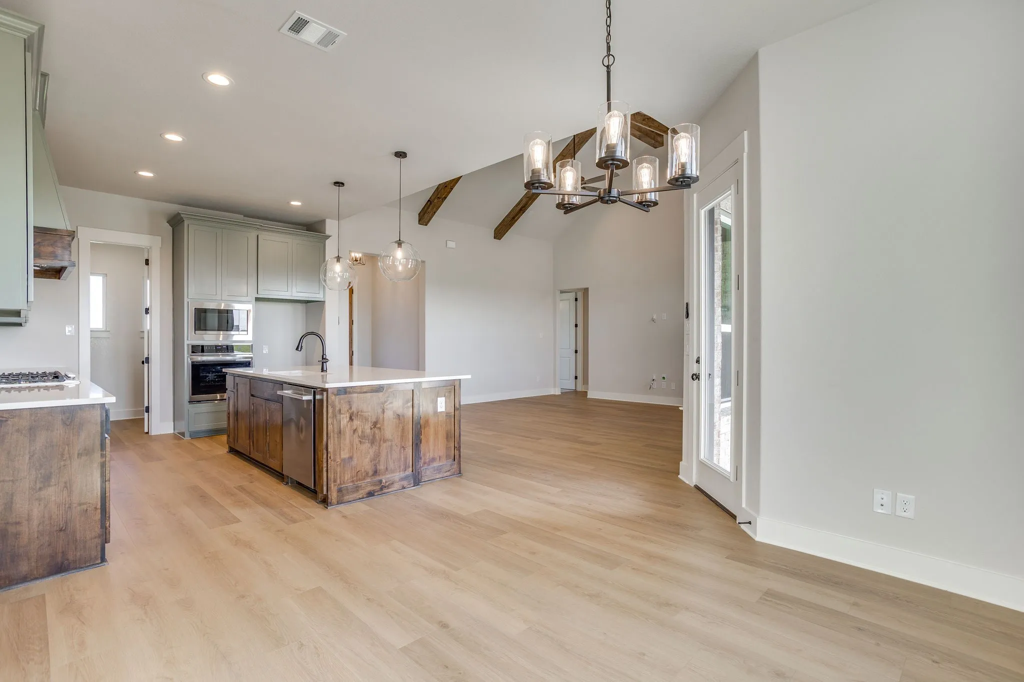 Light wood-finish flooring throughout, vaulted ceiling with exposed wood beams, and a modern chandelier
