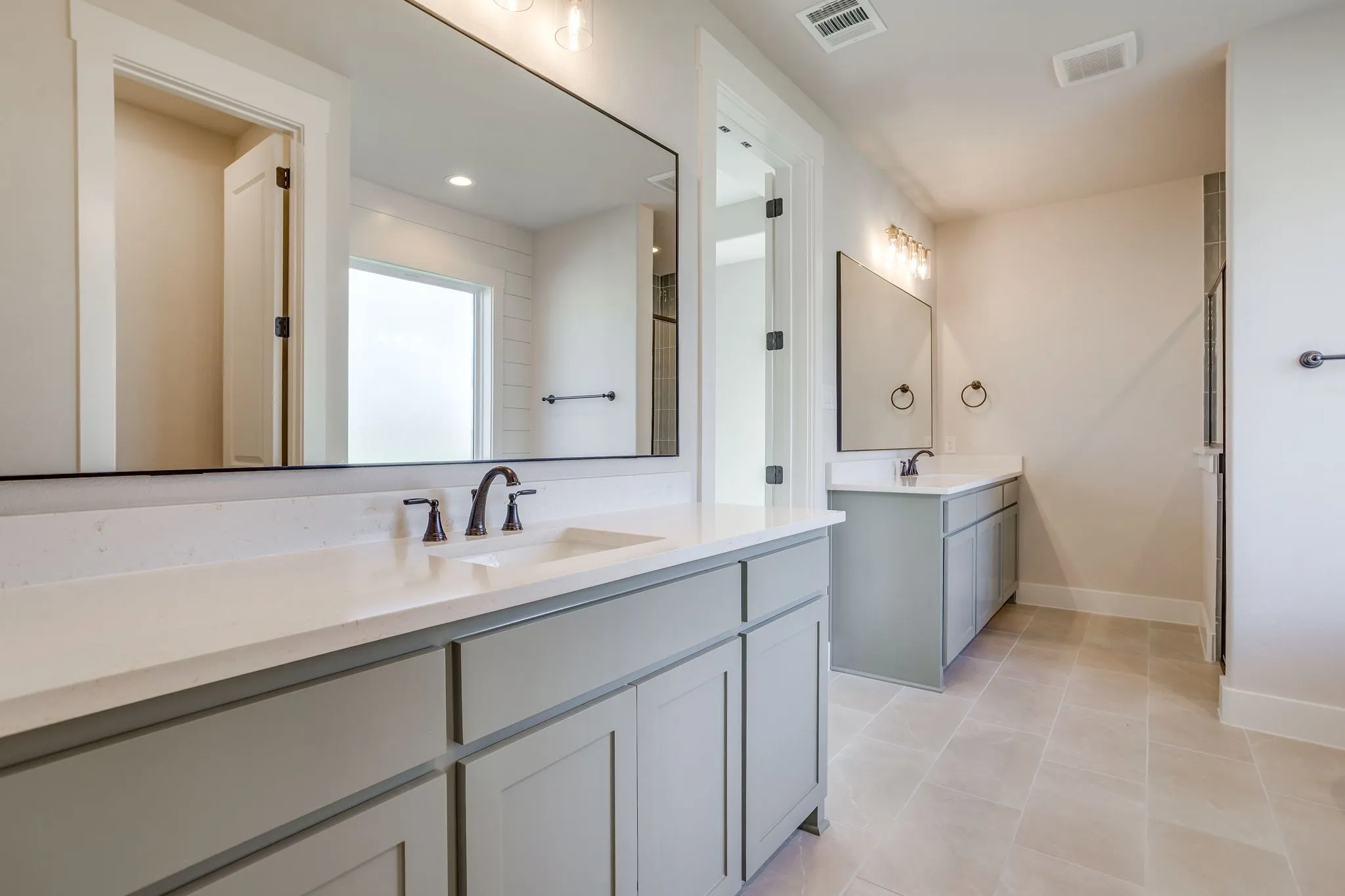 Dual vanities featuring light gray cabinetry and white countertops