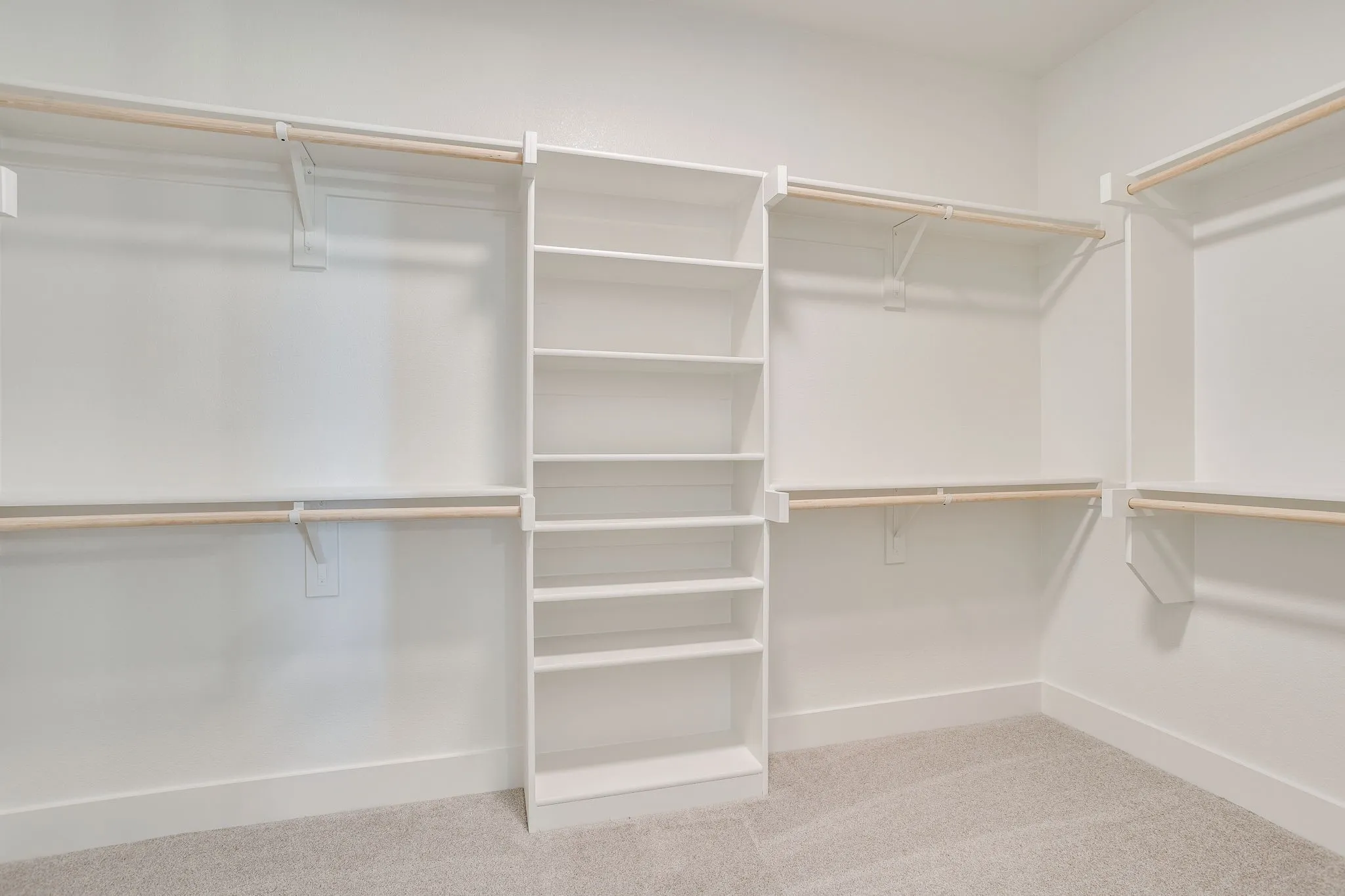 Walk-in closet featuring white built-in shelving, multiple hanging rods, and light-colored carpeting