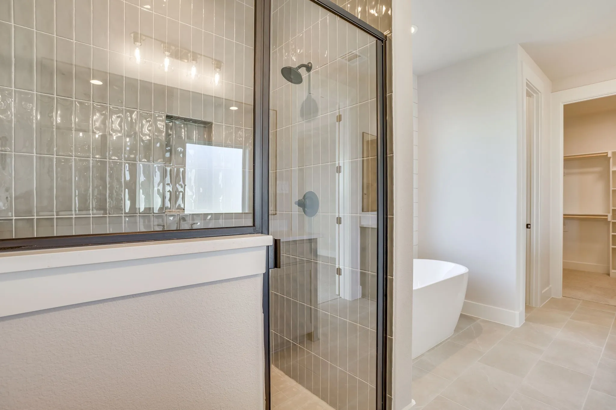 Glass-enclosed shower with dark trim, vertical subway tile, and a rainfall showerhead