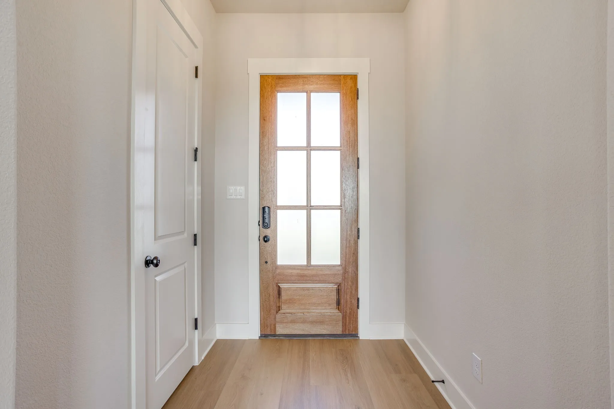 Wood-finish flooring, white trim, solid core interior door, and a six-lite wood entry door