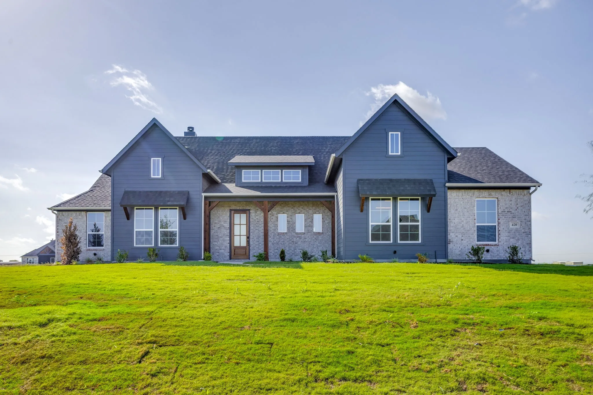 Exterior features include a combination of light-colored brick and blue siding, a dark shingled roof, a covered porch entry with wooden support beams, and multiple pane windows