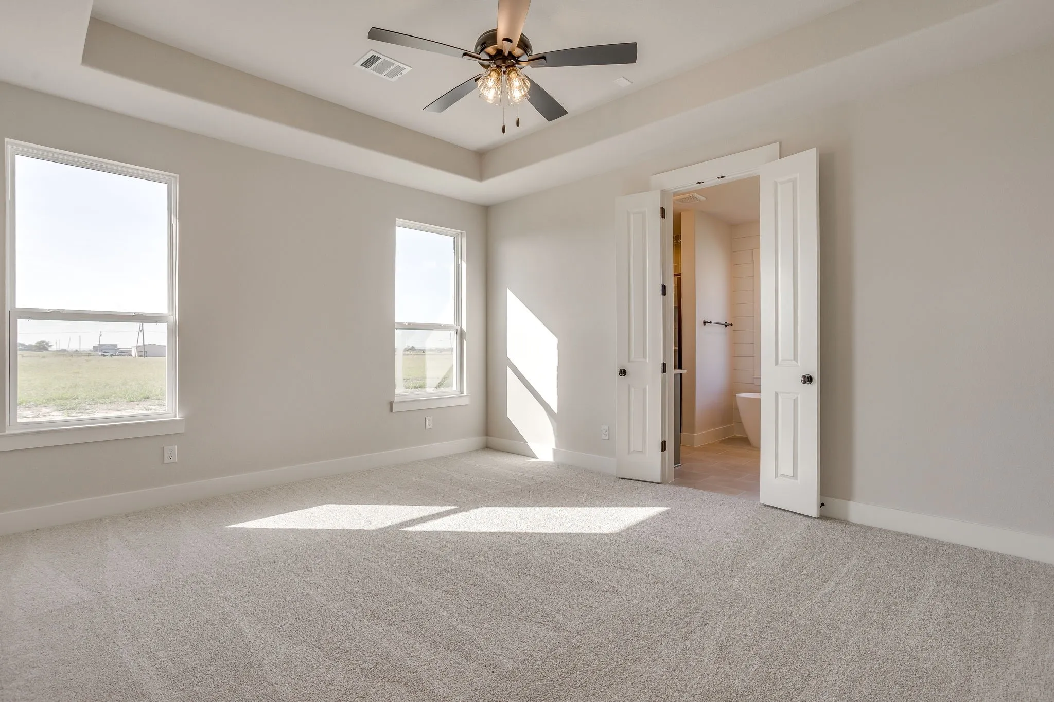Tray ceiling with a ceiling fan, two windows, and light-colored carpeting