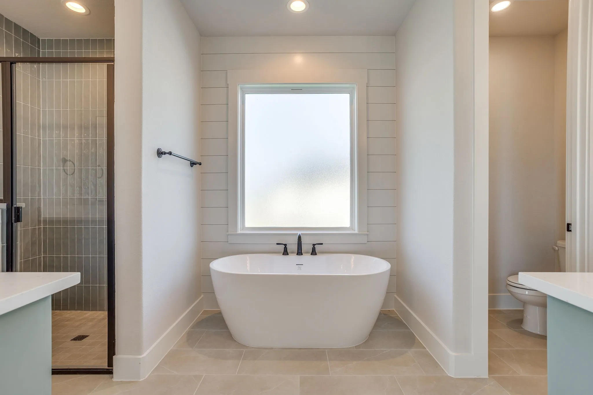 Freestanding soaking tub with matte black fixtures, set against a shiplap accent wall with a frosted window