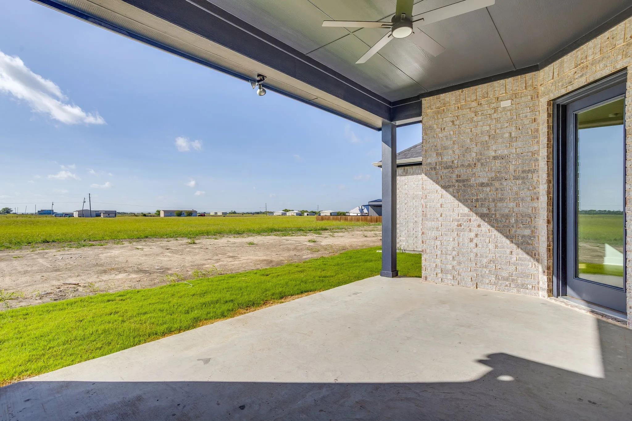 Covered concrete patio with ceiling fan, brick exterior, and a glass-paneled door