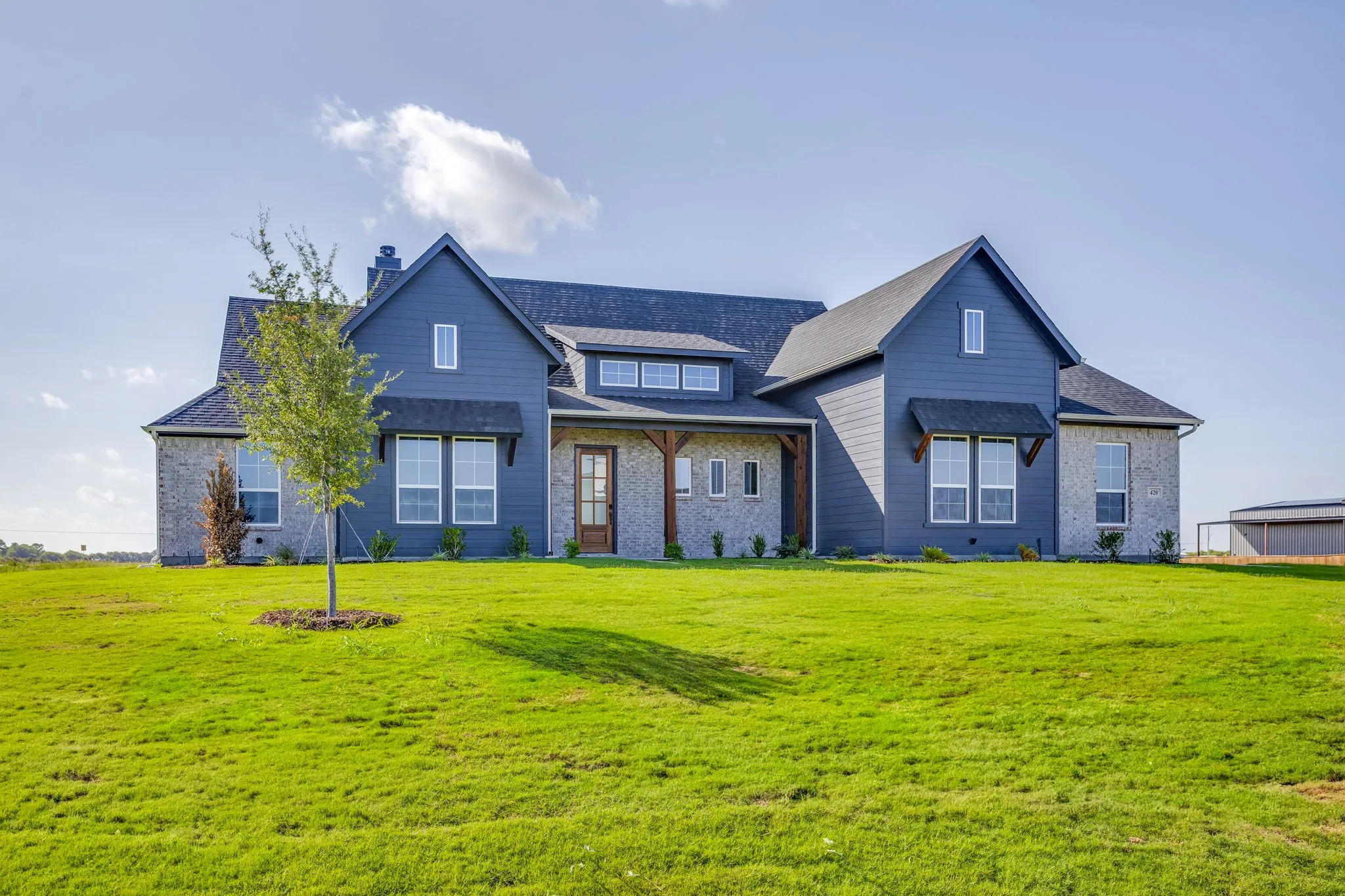 Spacious exterior featuring a combination of stone and siding, a dark asphalt shingle roof, multiple white-framed windows, and a prominent front door with a transom window