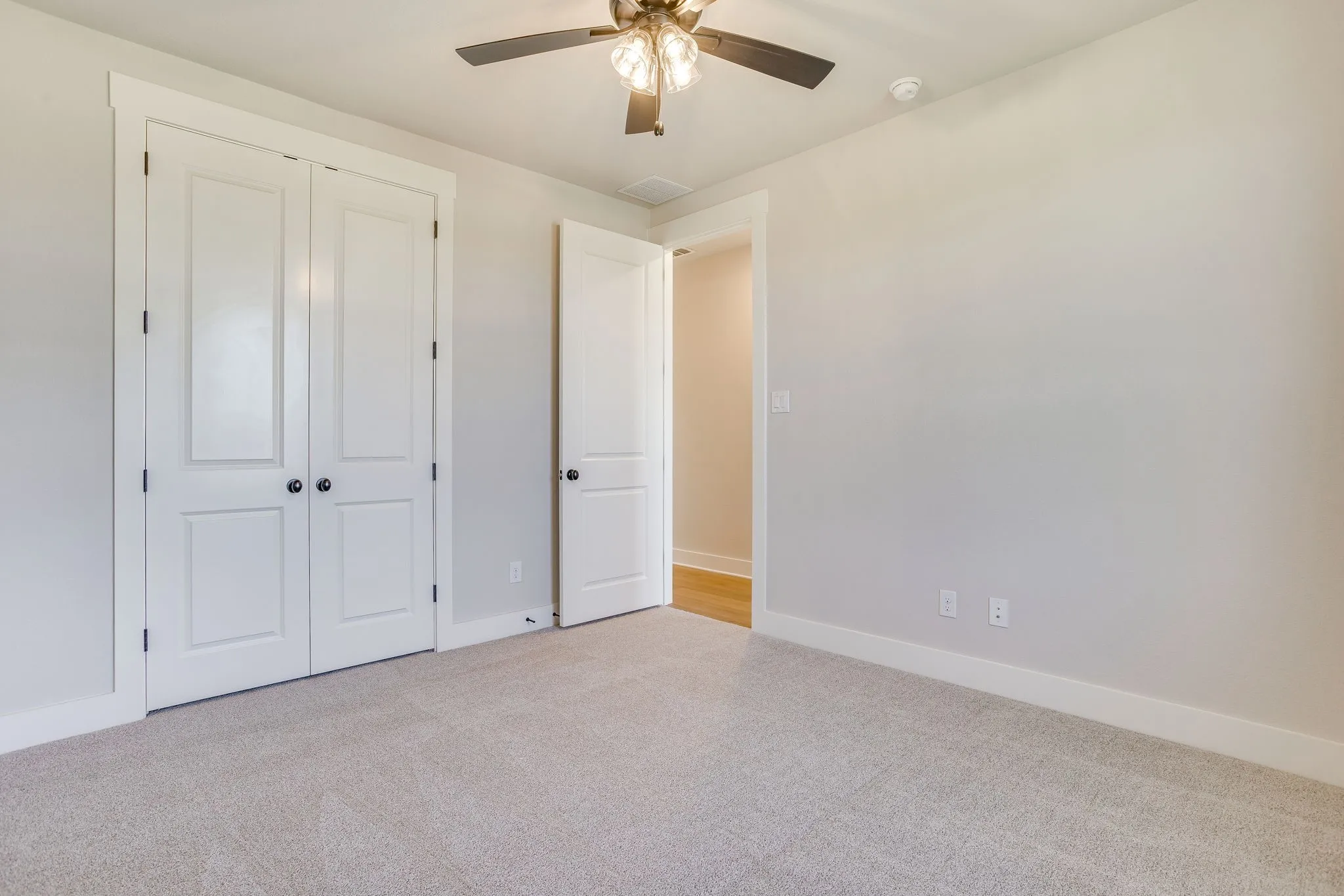 Neutral wall paint, carpeted flooring, ceiling fan with light, white paneled bifold closet doors, and white paneled interior door
