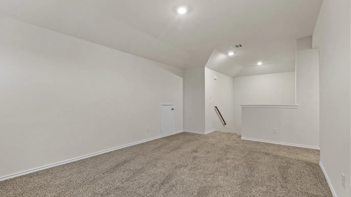 Carpeted interior space featuring white walls, recessed lighting, and a white railing with a dark wood handrail