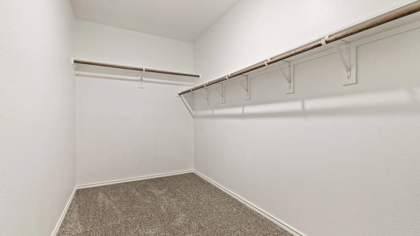 Spacious walk-in closet featuring neutral carpet flooring, chrome rod system with multiple hanging sections, and wire shelving for organized storage