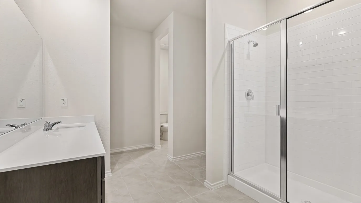 Glass-enclosed shower with white subway tile surround, single vanity with white countertop, chrome faucet, and tile flooring