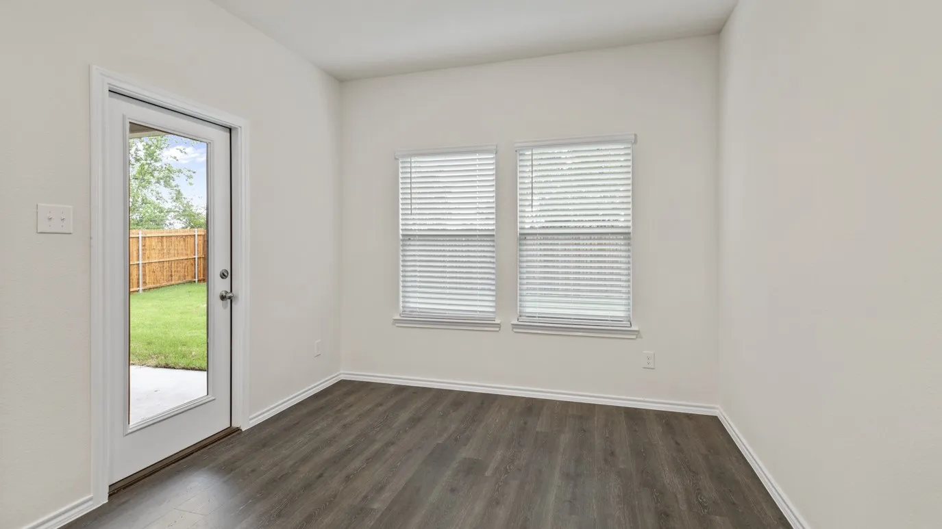 Wood-finish flooring with white baseboards, two windows with blinds, and a glass-paneled door leading to a patio and fenced yard