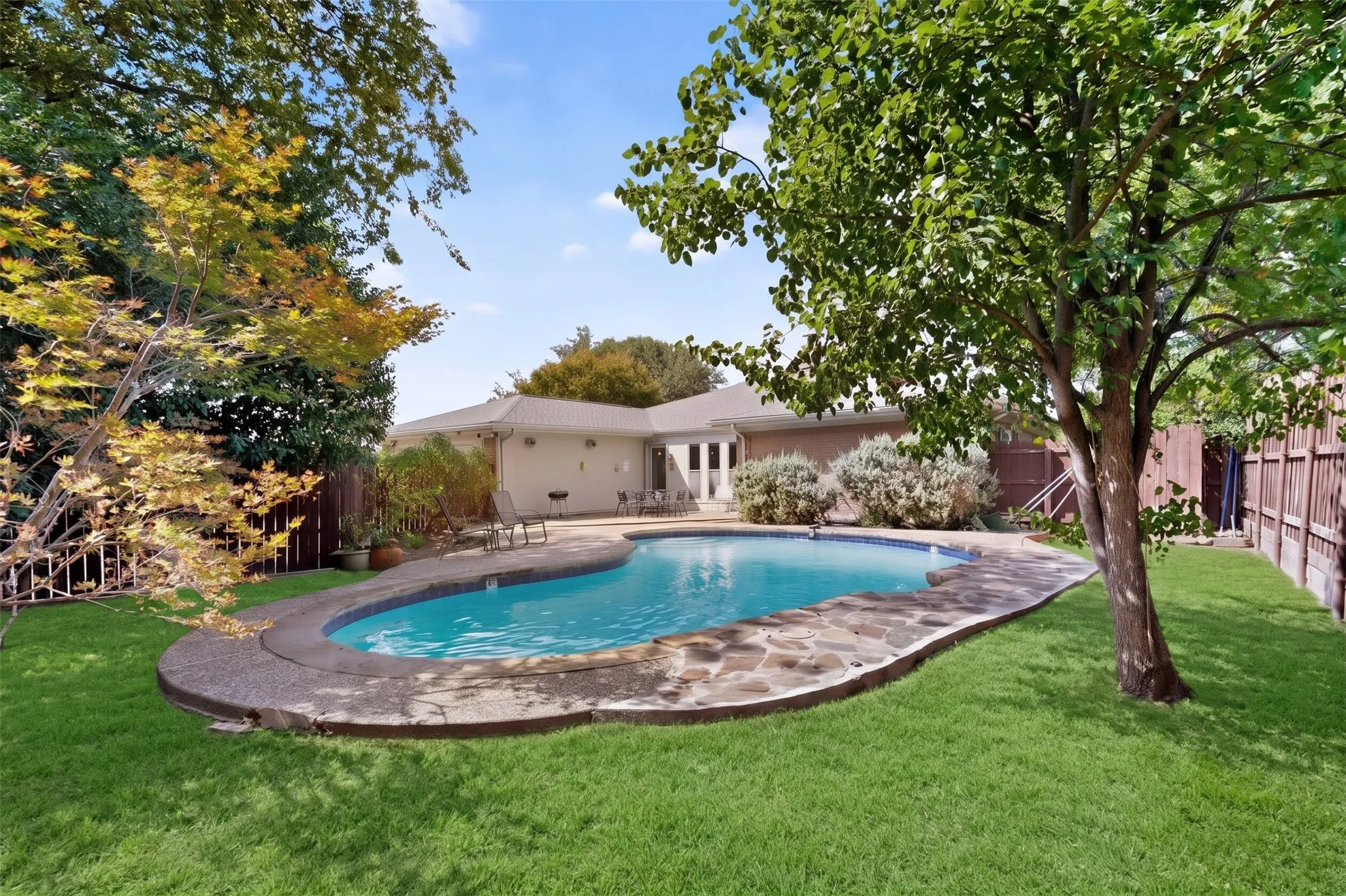 Expansive backyard with a curved swimming pool, flagstone coping, and a surrounding lawn (grass virtually enhanced)