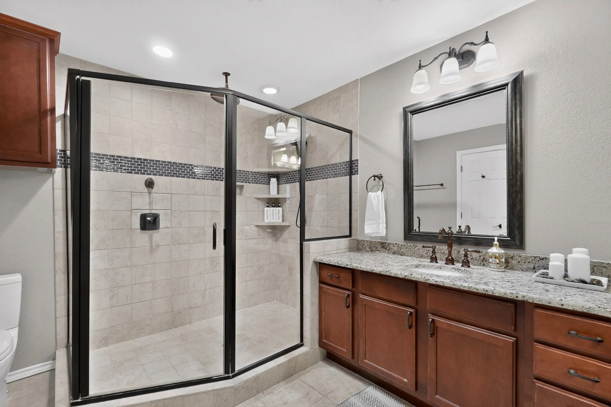 Enclosed shower with black frame, built-in shelving, and accent tile band