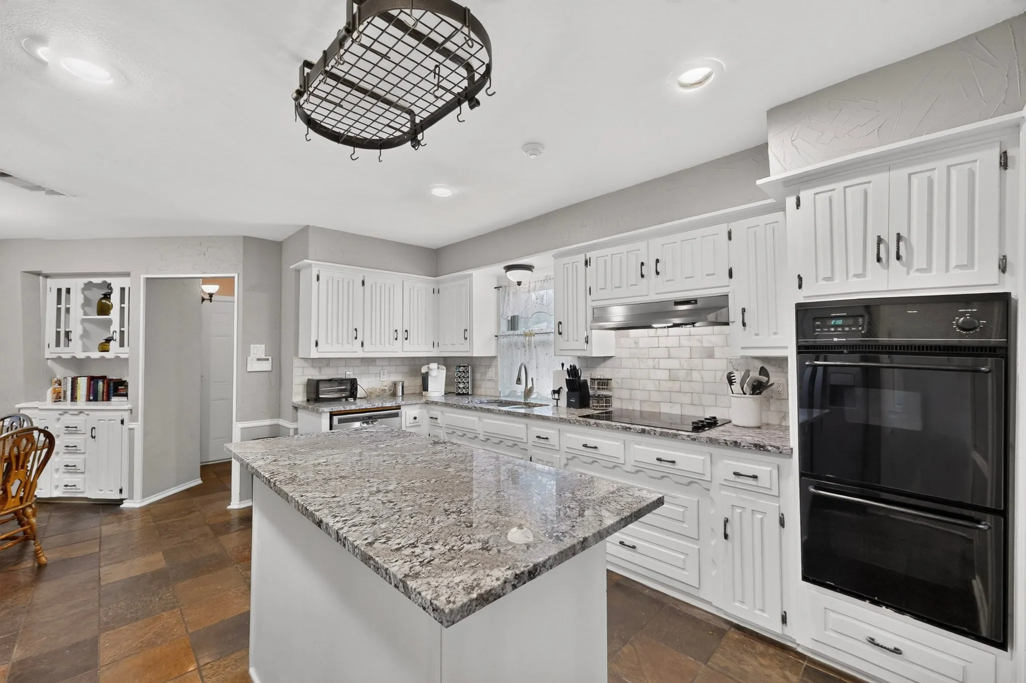 Kitchen featuring a center island with granite countertop, white cabinetry with dark hardware, subway tile backsplash, and built-in double ovens