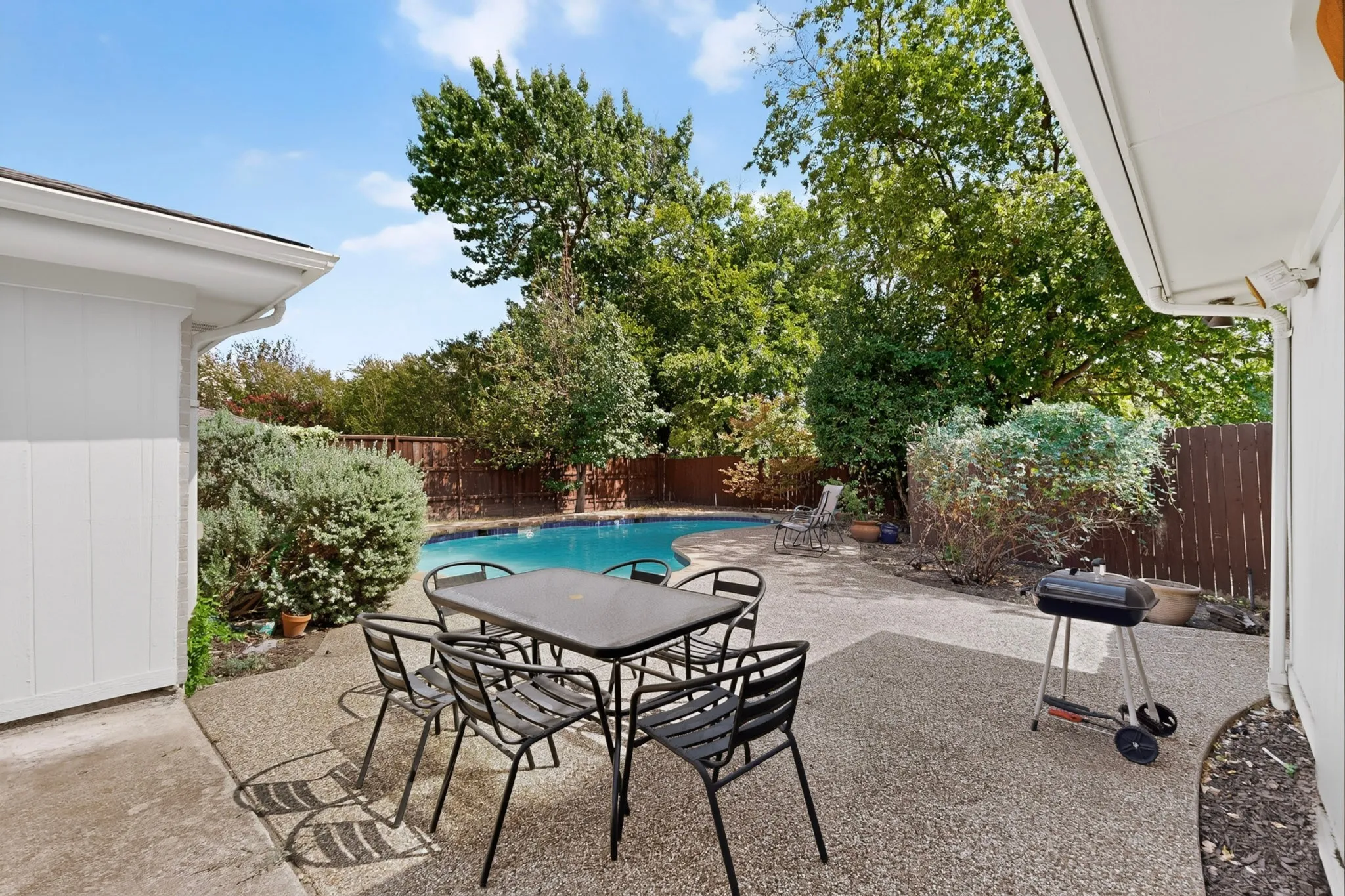 Expansive patio area with a built-in swimming pool, surrounding shrubs, and a privacy fence