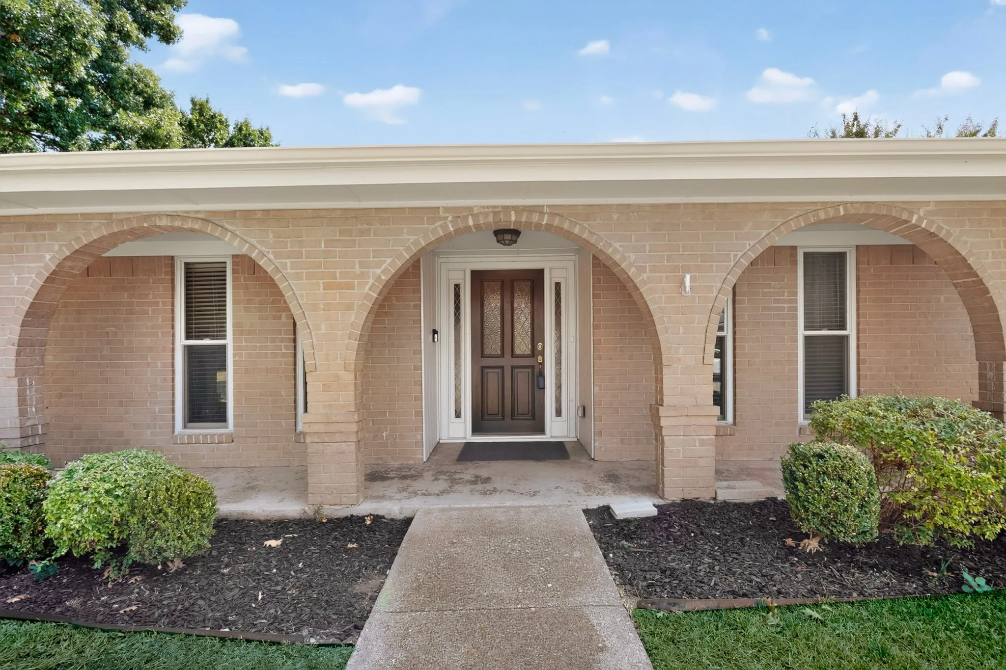 Brick exterior with arched entryways, a wood-paneled front door with glass inserts, and a concrete pathway