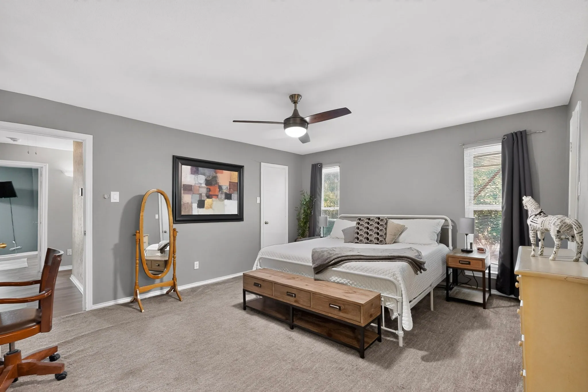 Expansive room featuring a ceiling fan with integrated lighting, multiple windows, and a doorway opening to an adjacent space
