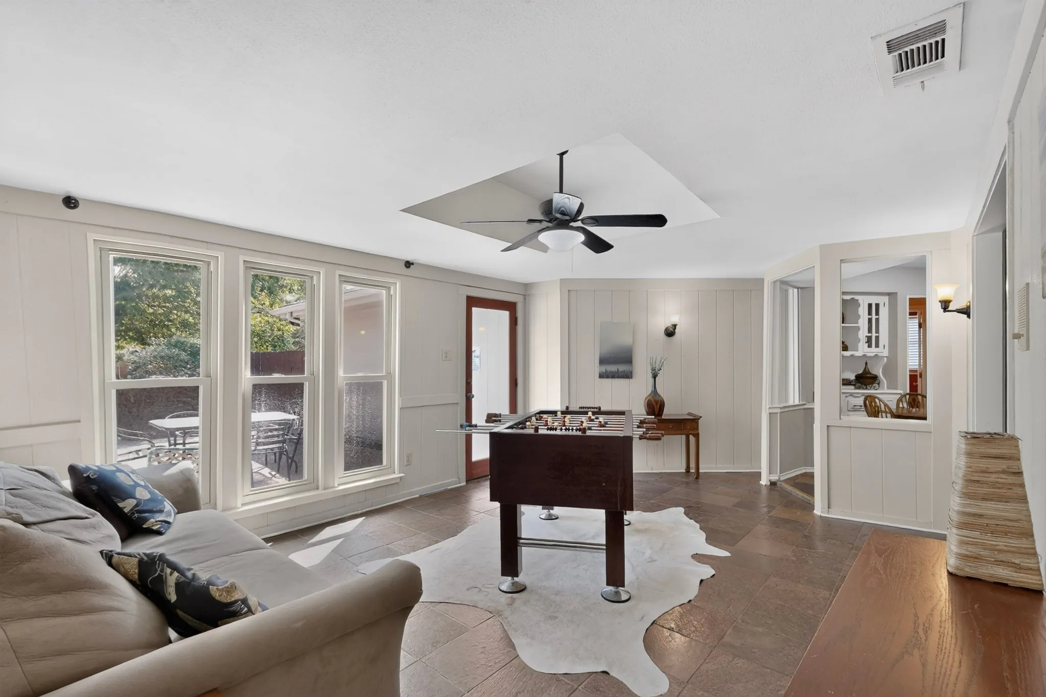 Tray ceiling with a ceiling fan, multiple large windows, paneled walls, and wood-finish flooring