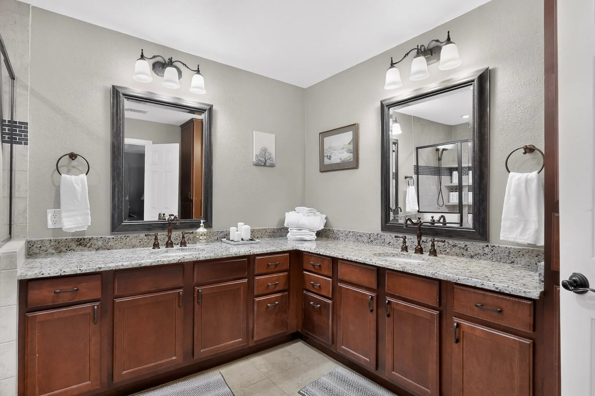 Double vanity with granite-style countertops, wood-finish cabinetry, and two framed mirrors